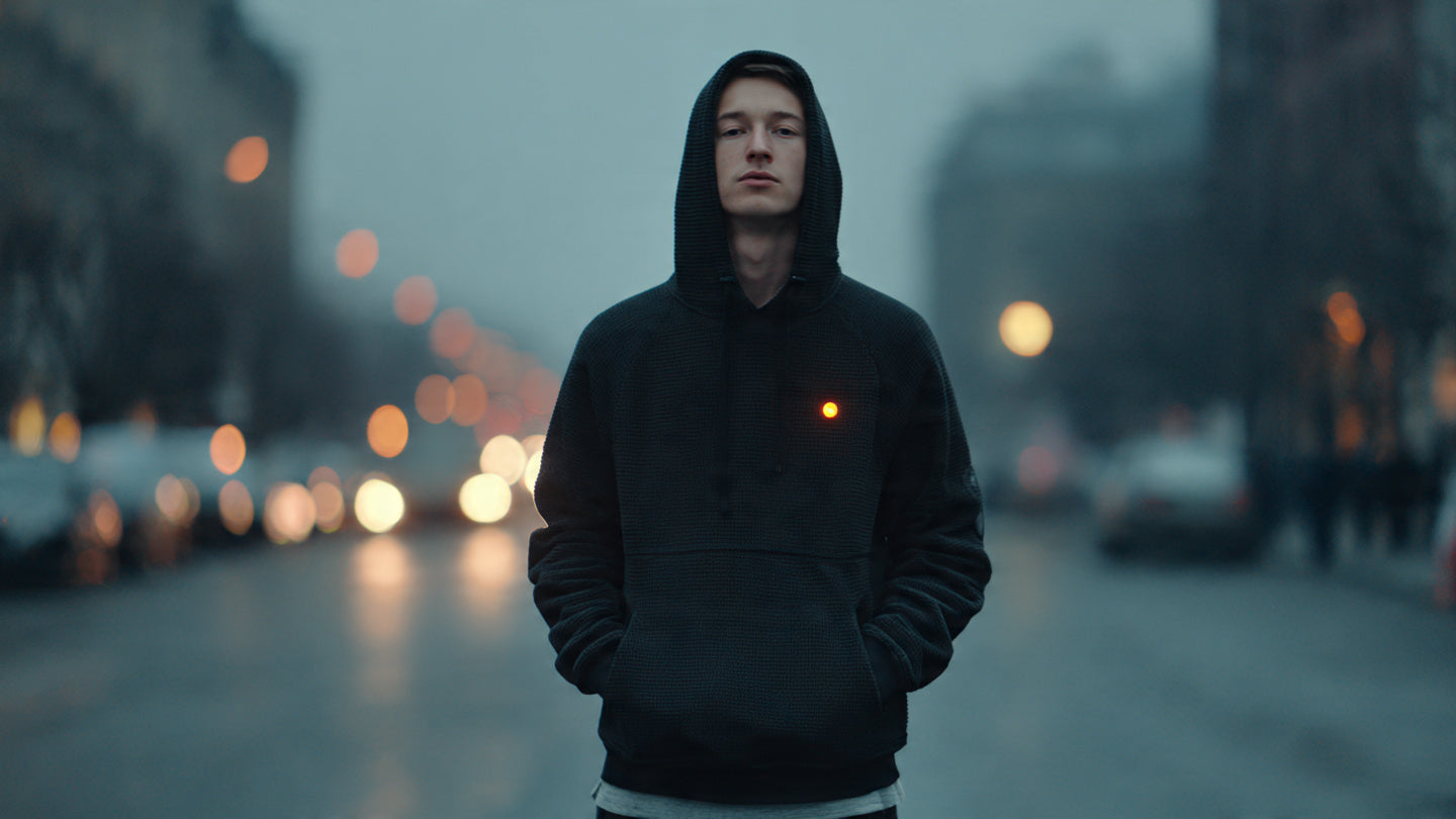 Person wearing a heated-style sweatshirt glowing warmly on a cold city street at dusk